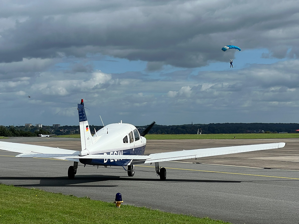 Weißes Flugzeug mit Fallschirmspringer im Hintergrund